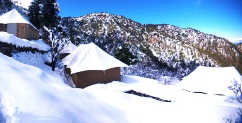 two tents covered in snow in front of a mountain at The Bugyal in Kanatal