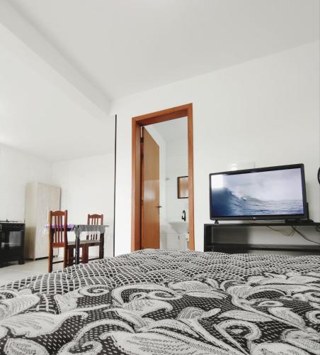 a bedroom with a bed and a flat screen tv at Suítes do Vale - Praia do Rosa in Imbituba