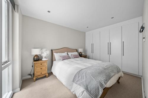 a white bedroom with a large bed and a night stand at Captivating 3-Bed House in London Holland Park in London