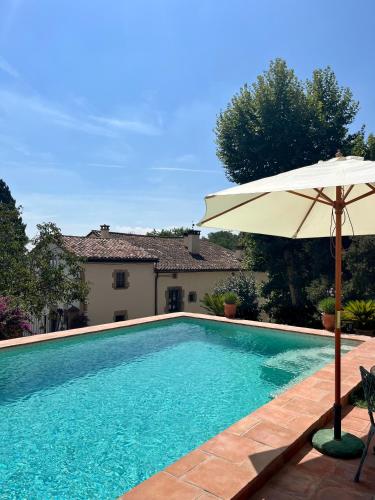 a swimming pool with an umbrella and a house at Masia Can Viver - Olive oil tourism B&B in Bigues i Riells