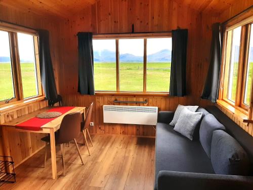 a living room with a couch and a table and windows at Lambhus Glacier View Cabins in Höfn