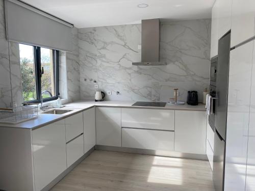 a white kitchen with white cabinets and a window at Casa da Zéfinha - Villa, em Cinfães, no Douro in Cinfães