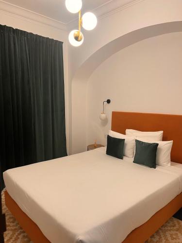 a bedroom with a large white bed with green curtains at 145 Townhouse in Ílhavo