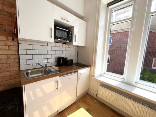 una cucina con armadi bianchi, lavandino e finestra di Flat 12, 10 St John’s Road a Bournemouth