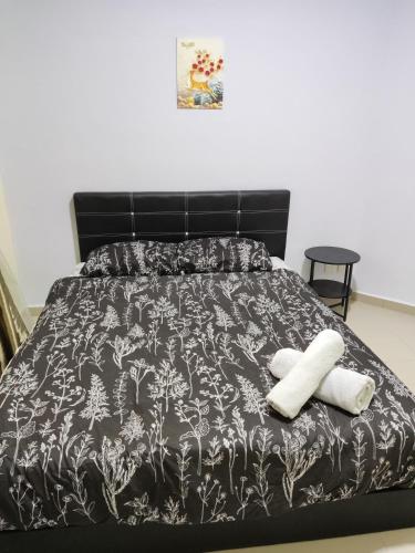 a bed with a black and white comforter and two towels at JoJo Homestay Tiara Residence in Desaru