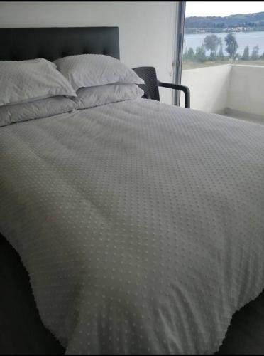 a bed with a white comforter and pillows at Apartamento con vista al lago. in Paipa