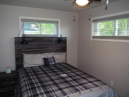 a bedroom with a bed with a wooden headboard and two windows at Manist-easy - Lakefront With Dock And Kayaks! in Kalkaska
