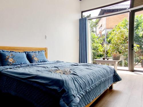a bedroom with a blue bed and a large window at Homestay Vườn Trái Cây Nhiệt Đới VÔ ƯU GARDEN in Bao Loc