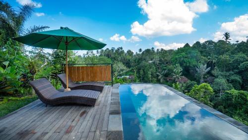 a pool with chairs and an umbrella next to a wooden deck at Anja Villas Ubud in Tegalalang