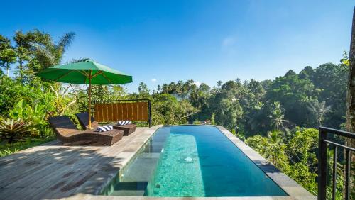 a pool with chairs and an umbrella next to a resort at Anja Villas Ubud in Tegalalang