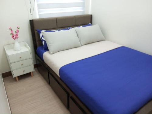 Cama pequeña con sábanas azules y blancas y mesita de noche en Osam Empire Suites 2BR Staycation at Trees Residences Condominium, en Manila