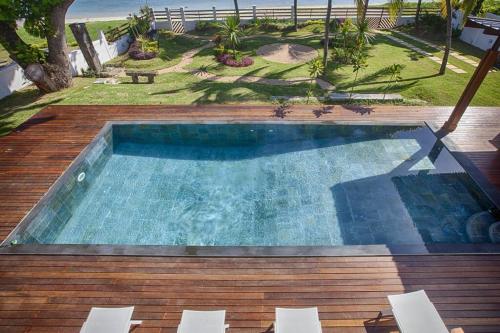 a swimming pool on a wooden deck with chairs and the beach at Villa luxueuse - Pointe aux Sables in Pointe aux Sable