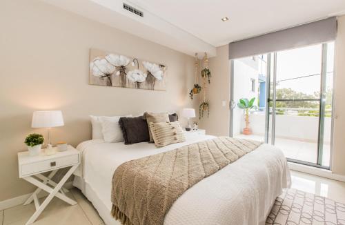 a white bedroom with a bed and a window at Lakeview luxury apartment in The Entrance