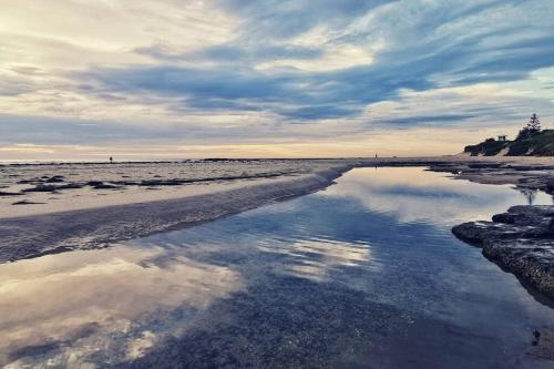 a beach with a reflection of the sky in the water at Waterview luxury hideaway, 2 min walk to all, pool in The Entrance