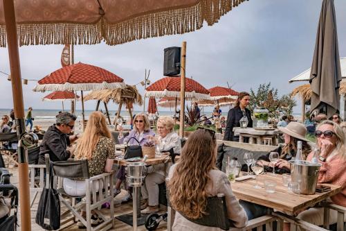 B&B de Drukkerij Zandvoort - luxury private guesthouse في زاندفورت: مجموعة من الناس يجلسون على الطاولات على الشاطئ