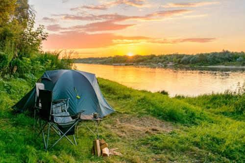 une tente sur la rive d'une rivière au coucher du soleil dans l'établissement A&G SODYBA CAMP žvejų kampelis, à Plungė