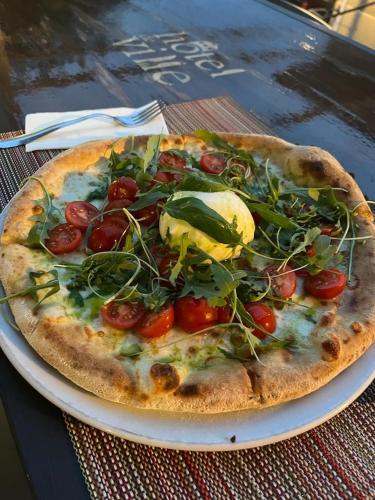 a pizza with tomatoes and greens on a plate on a table at Hotel de ville d'Yvonand in Yvonand