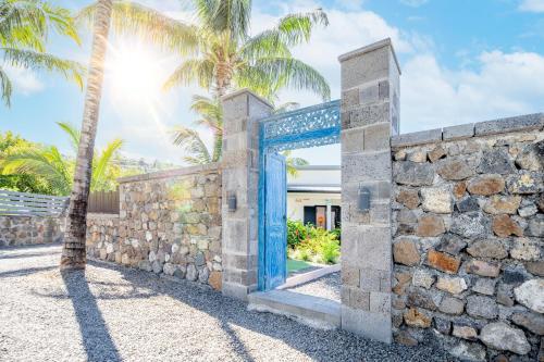 an entrance to a stone wall with a blue door at Ô Ruisseau Lodges - Lodge Dattier in Saint-Louis
