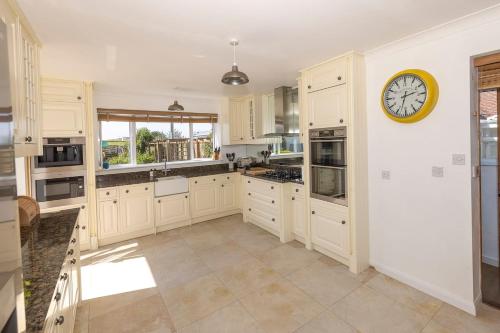 a kitchen with white cabinets and a clock on the wall at Big Sky at Hive Beach in Burton Bradstock