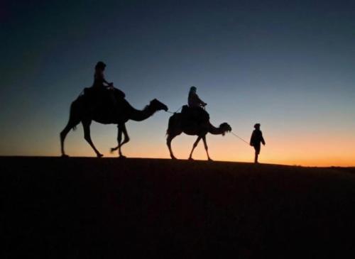 two people riding camels in the desert at sunset at Unique sahara camp in Merzouga