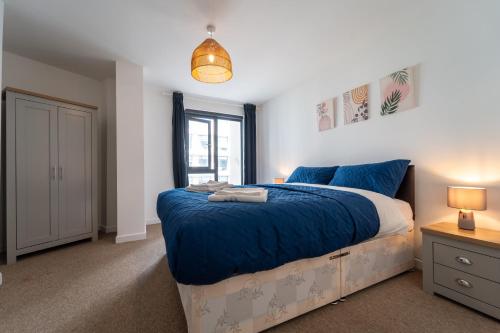 - une chambre dotée d'un grand lit avec des draps bleus et une fenêtre dans l'établissement Spacious Apartment in Woking Town Centre, à Woking