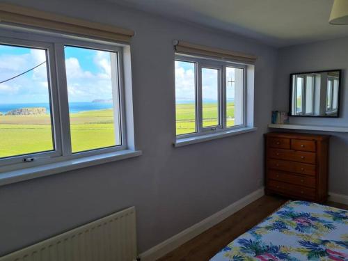 a bedroom with three windows and a bed and a dresser at Ballintoy house with great sea views in Ballintoy