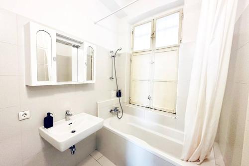 a white bathroom with a sink and a tub and a window at Best Location - Cozy City Centre Apartment in Vienna