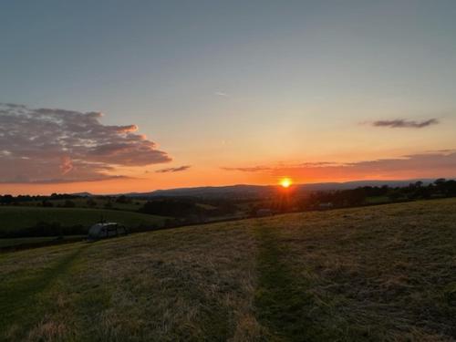 a sunset in a field with the sun in the distance at Little Middop Farm Camping Pods in Gisburn