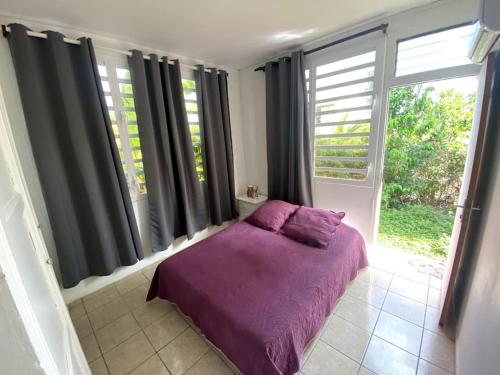 a bedroom with a purple bed in front of windows at La Villa Ti-Louise à Marie-Galante in Grand-Bourg