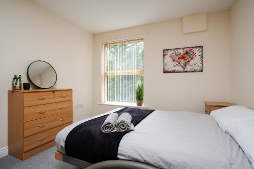 a bedroom with a bed and a dresser and a window at Brimmond Homes - nr to Univ, Hospitals, o2 Apollo, PLAB & 7 mins to City Centre - Stylish, Modern & Secure 2 Bed, 2 Bath Apt with Allocated Free Parking in Manchester