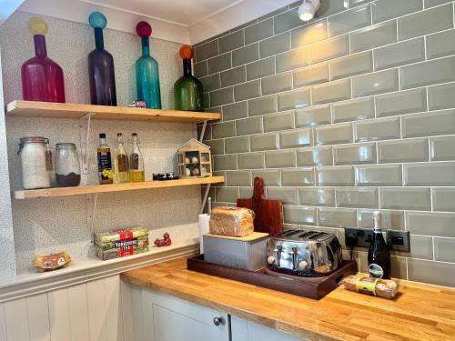 a kitchen counter with wine bottles on shelves at Olive Tree Cottage in Rye