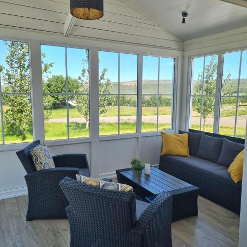 een woonkamer met een bank, stoelen en ramen bij Cosy cottage in the countryside in Þingeyjarsveit