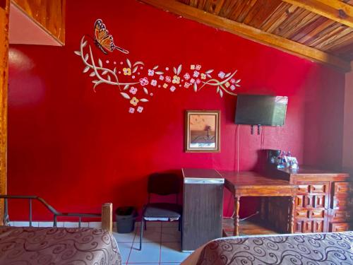 a bedroom with a red wall with a desk and butterflies on the wall at Hotel Real de la Sierra in Mazamitla
