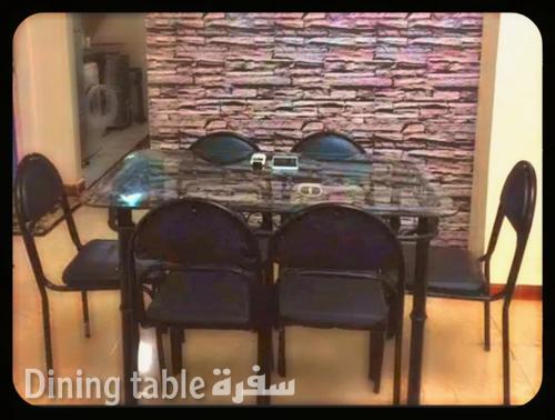 einen Esstisch mit Stühlen und eine Steinmauer in der Unterkunft Air-conditioned apartment - شقة مكيفه للايجار ف ميامي in Alexandria