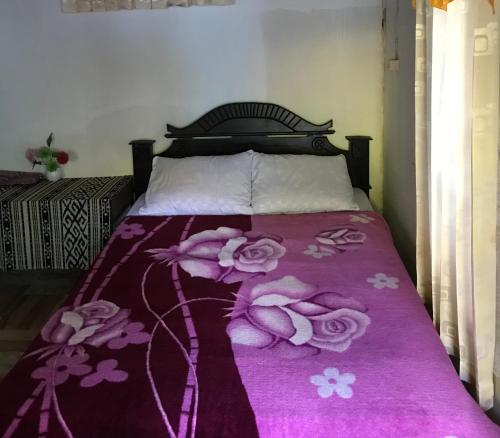 a bed with a purple bedspread with roses on it at Bungalow Paer Doe in Sembalunbumbung
