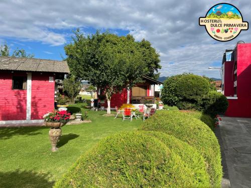 um jardim com sebes em frente a um edifício vermelho em Hotel Dulce Primavera em Ambato