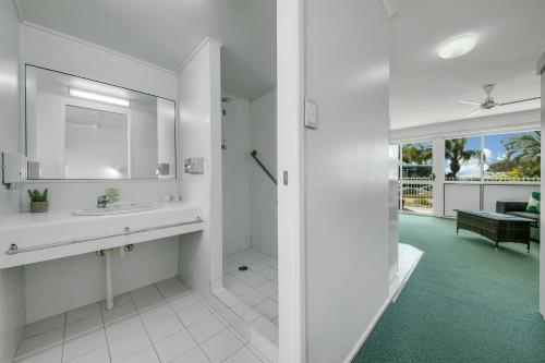 een witte badkamer met een wastafel en een spiegel bij Reef Adventureland Motor Inn in Tannum Sands