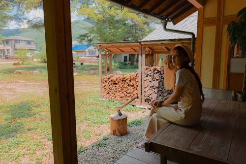 a woman sitting on a bench on a porch at 古民家オーベルジュmocca in Kokuryō