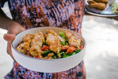 a person holding a bowl of chicken and vegetables at Kupaga Villas Boutique Hotel - Adults Only in Jambiani