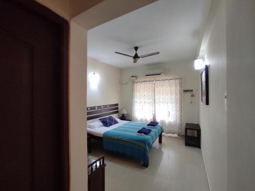 a bedroom with a bed with a blue blanket and a window at Beach Apartment 2,COLVA , GOA, INDIA in Colva