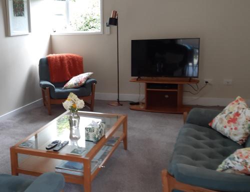 uma sala de estar com uma televisão e duas cadeiras e uma mesa em Bunny Cottage em Masterton