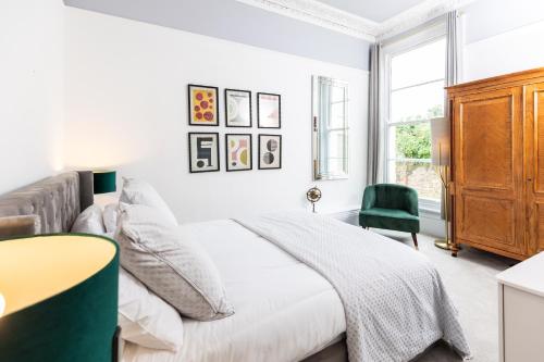 a white bedroom with a bed and a green chair at 10 Sydenham - By Luxury Apartments in Cheltenham
