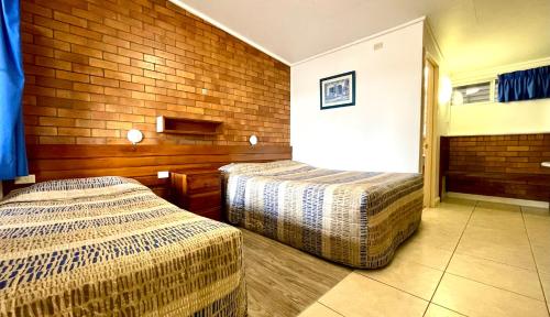 two beds in a room with a brick wall at Motel Myall in Dalby