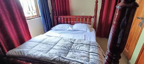 1 cama en un dormitorio con cortinas rojas en cosy living, en Gulu