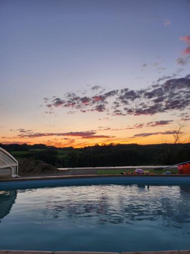 une piscine avec un coucher de soleil en arrière-plan dans l'établissement Le Point du Jour, à La Grandville