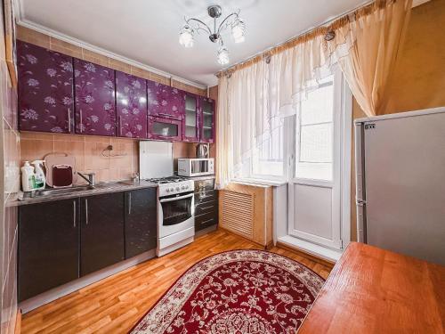 una cocina con armarios morados y una gran ventana en Тасс уютная квартира в центре города, en Petropavlovsk