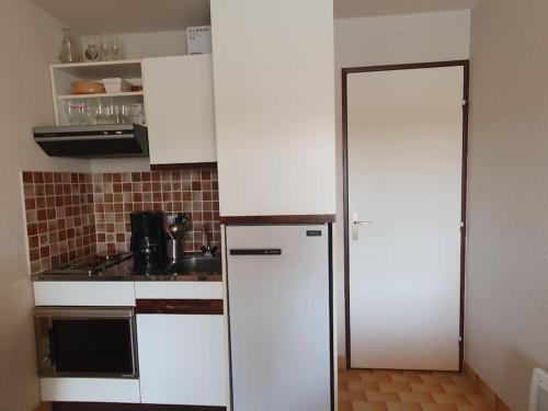  La cuisine est équipée de placards blancs et d'un réfrigérateur. dans l'établissement Studio cabine La Lagune Côté Espiguette, au Grau-du-Roi