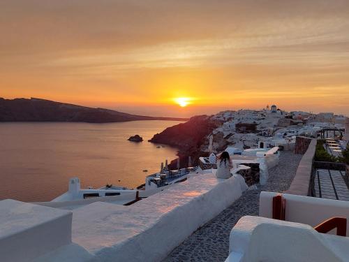 a sunset over the ocean with a group of buildings at Olympic Villas in Oia