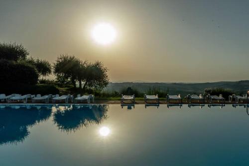 a pool with chairs and the sun in the background at AffittiBreviSiena - Palazzo Monaci Appartamento con piscina nelle crete Senesi in Asciano