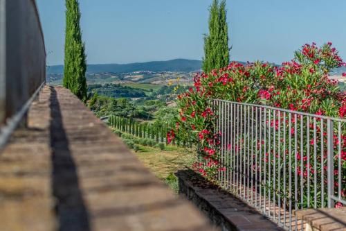 a fence with red flowers and trees on a hill at AffittiBreviSiena - Palazzo Monaci Appartamento con piscina nelle crete Senesi in Asciano